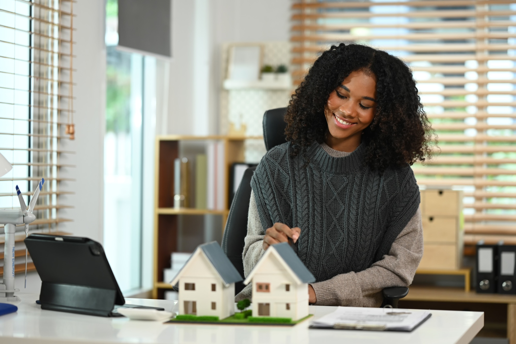 Woman holding a house model and wind turbine representing sustainable housing and clean energy